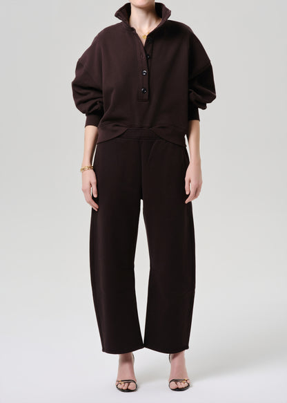 A model wearing a dark brown two-piece set consisting of a long-sleeve buttoned top and matching wide-leg cropped pants, paired with clear high-heeled sandals against a grey background.