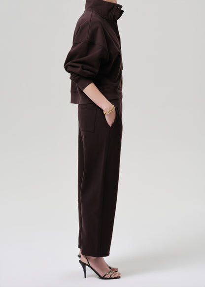 A model shown from the side wearing a dark brown cropped jacket and matching wide-leg trousers, paired with black high-heeled sandals against a grey background.