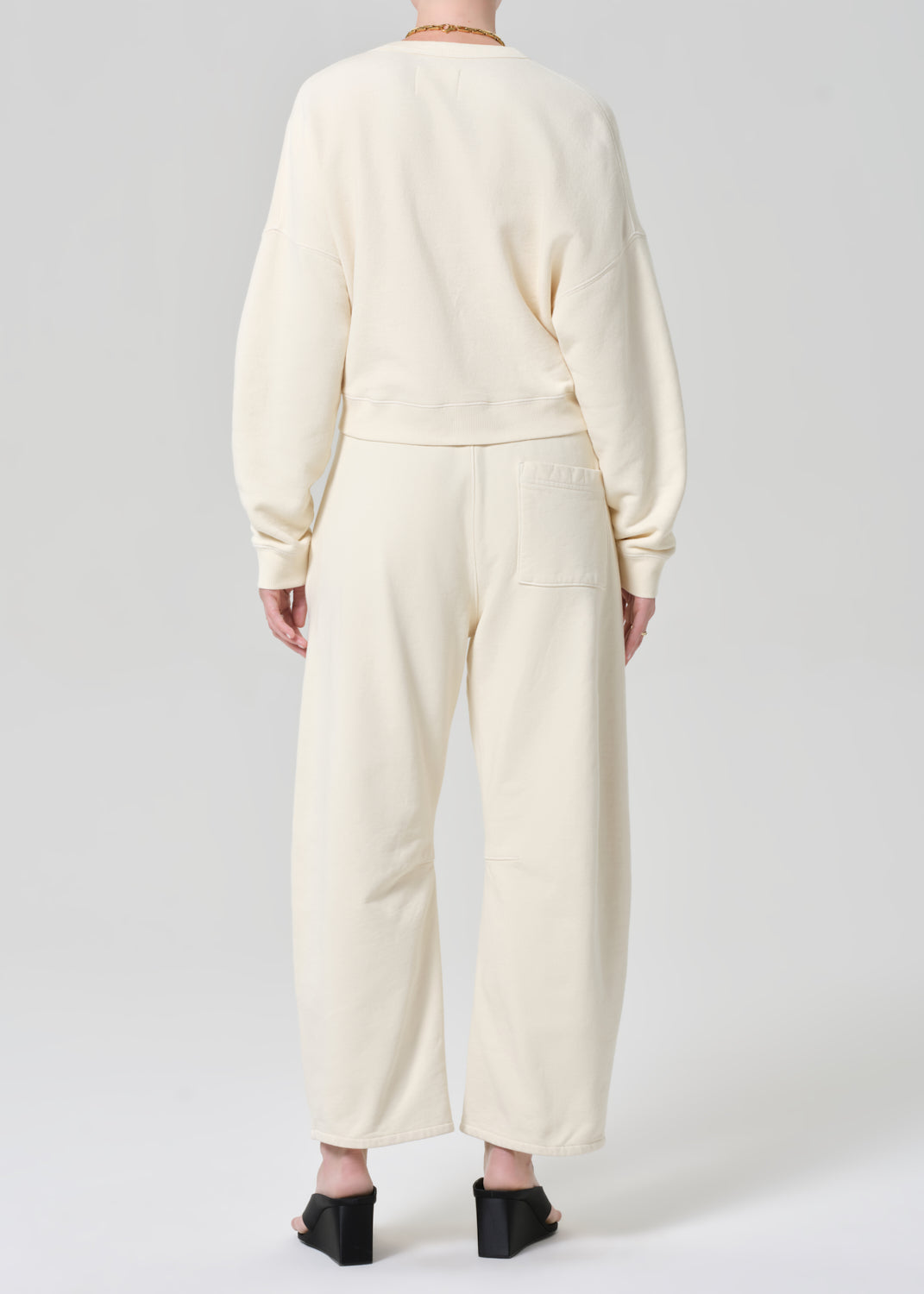 Person wearing a cream sweatshirt with matching cream sweatpants on a grey background