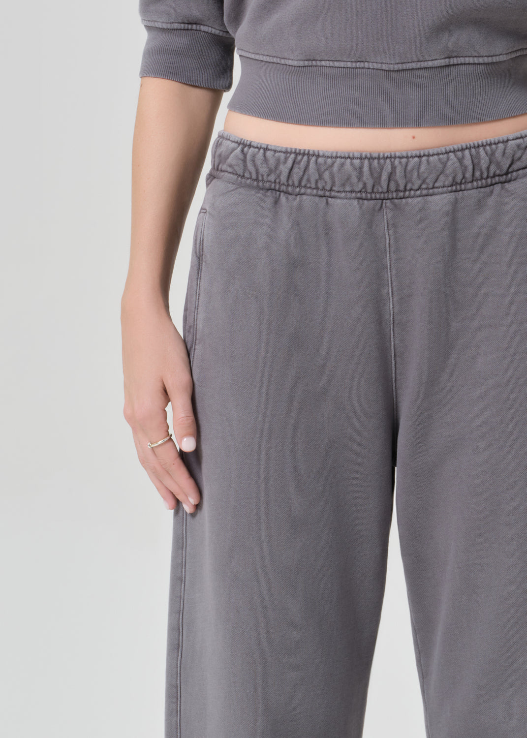 Person wearing a gray top with matching grey sweatpants on a grey background