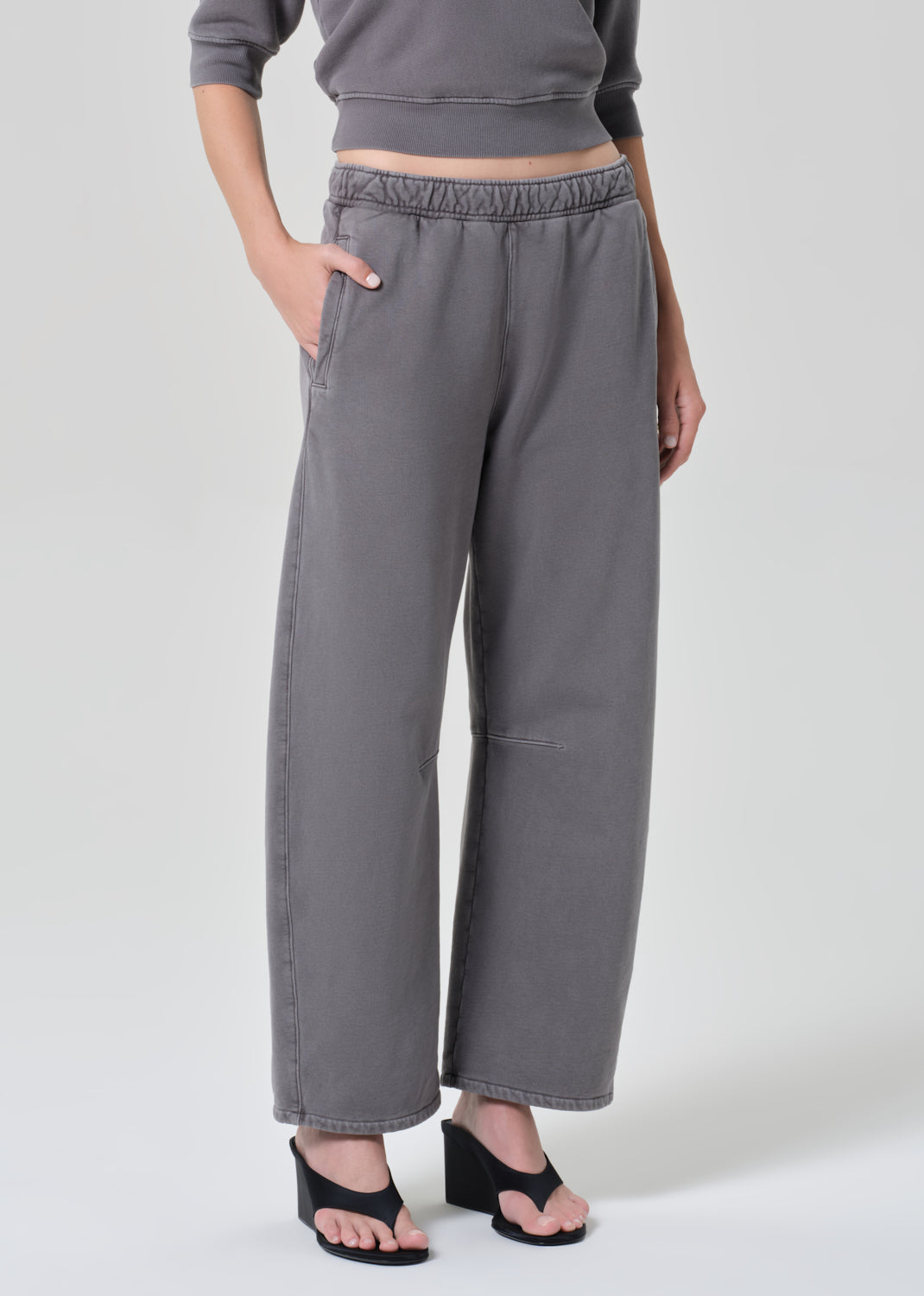 Person wearing a gray top with matching grey sweatpants on a grey background
