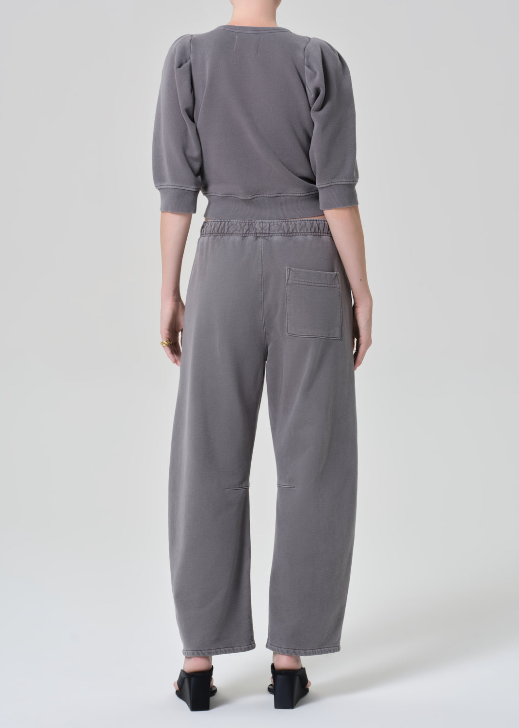 Person wearing a gray top with matching grey sweatpants on a grey background