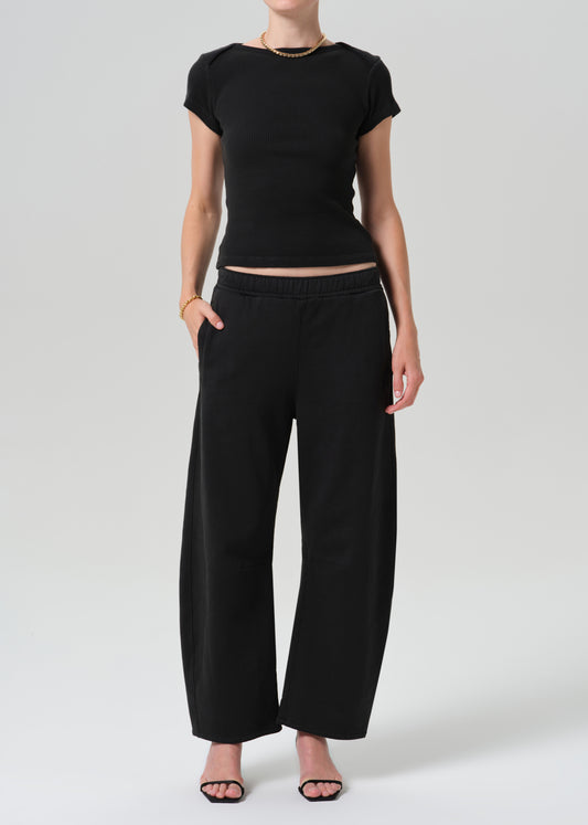 A model wearing a black short-sleeve cropped top and matching black wide-leg trousers, paired with black sandals, against a grey background.