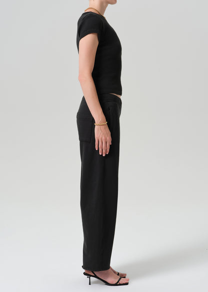 A model shown in profile wearing a black short-sleeve top and black wide-leg trousers, paired with black heeled sandals, against a grey background.