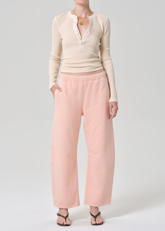 Person wearing a light peach top and pink sweatpants on a grey background