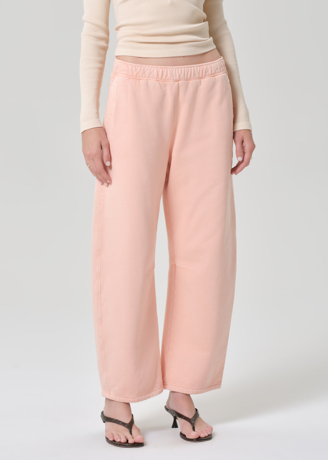 Person wearing a light peach top and pink sweatpants on a grey background