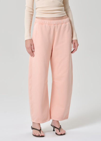 Person wearing a light peach top and pink sweatpants on a grey background