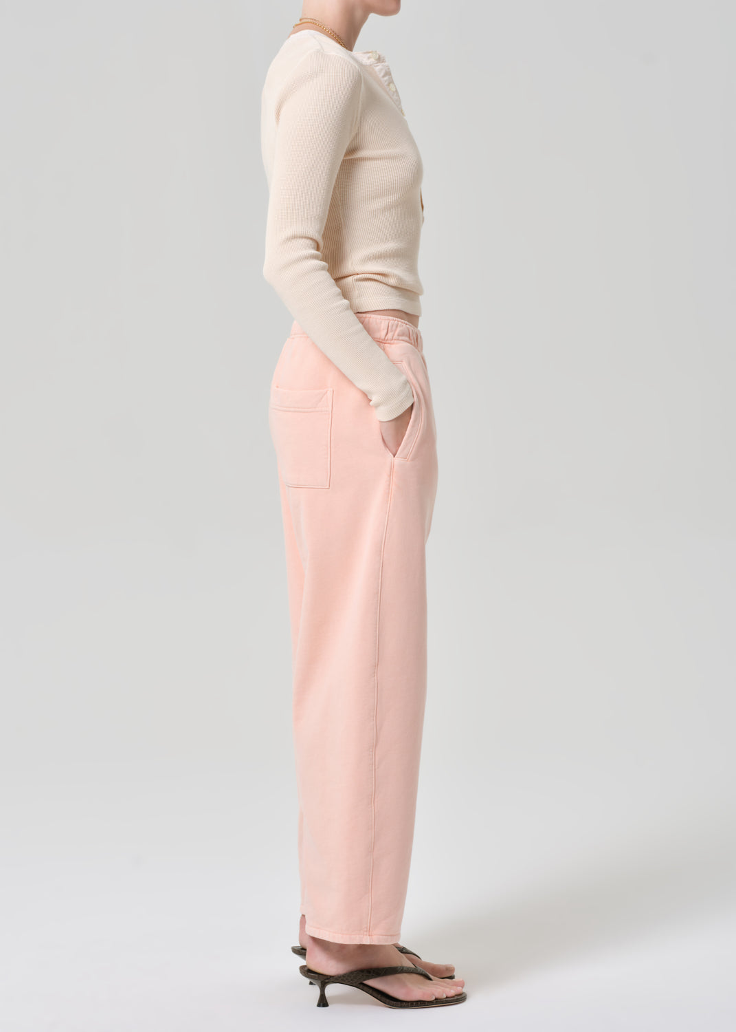 Person wearing a light peach top and pink sweatpants on a grey background