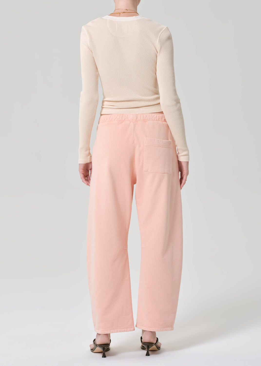 Person wearing a light peach top and pink sweatpants on a grey background