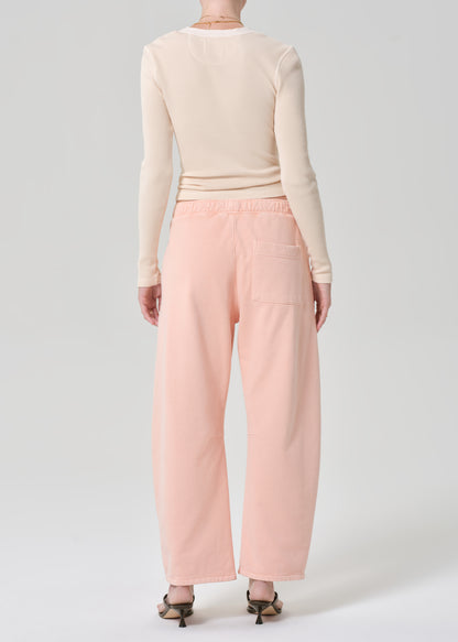 Person wearing a light peach top and pink sweatpants on a grey background
