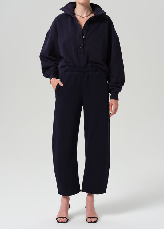 A model wearing a dark navy blue two-piece loungewear set consisting of a half-zip pullover hoodie and matching wide-leg cropped pants, styled with black heeled sandals against a grey background.