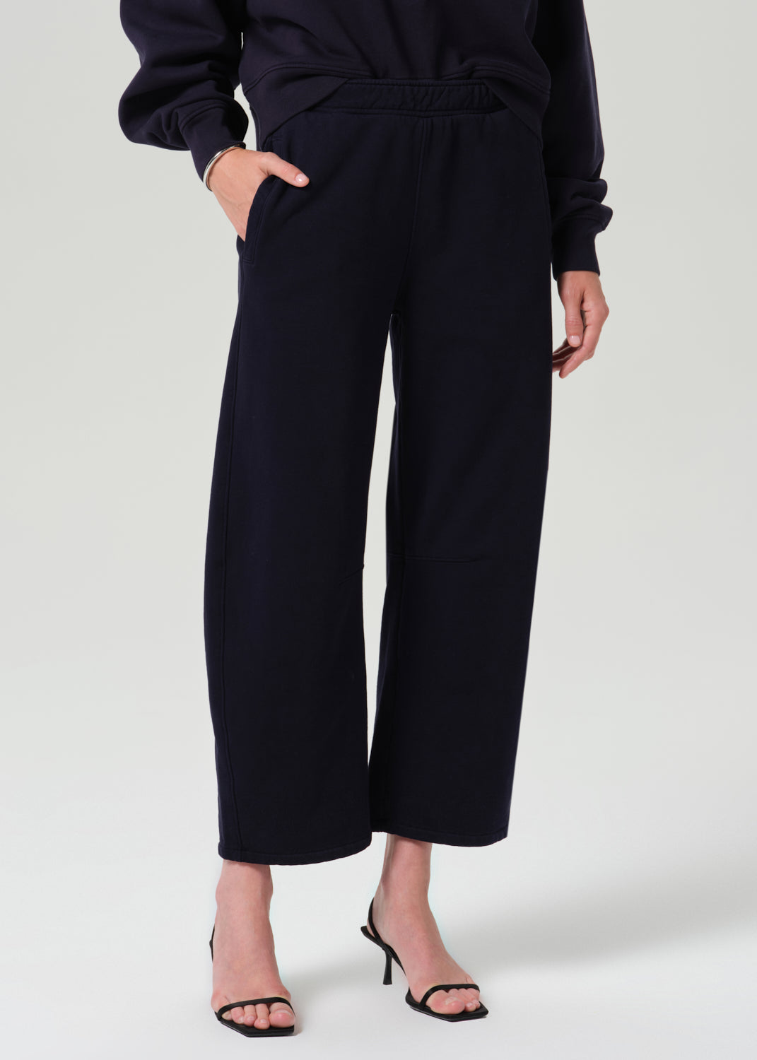 A model wearing dark navy wide-leg cropped trousers with an elastic waistband, paired with a matching dark top and black heeled sandals, against a grey background.