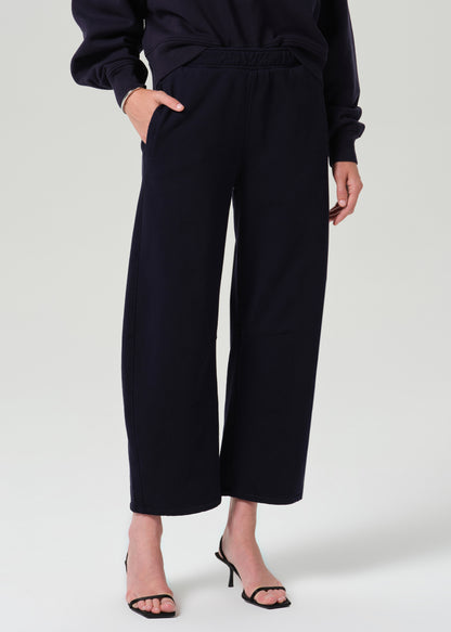 A model wearing dark navy wide-leg cropped trousers with an elastic waistband, paired with a matching dark top and black heeled sandals, against a grey background.