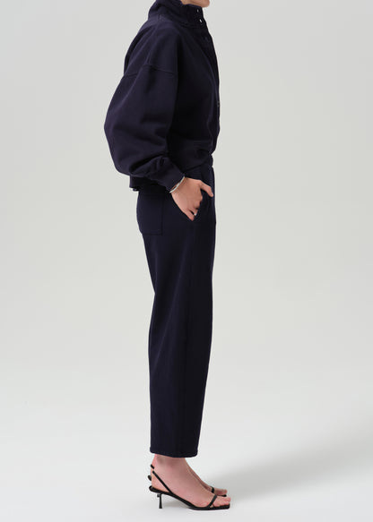 A model shown from the side wearing a dark navy blue two-piece set consisting of a cropped long-sleeve top and matching cropped trousers, paired with black heeled sandals against a grey background.