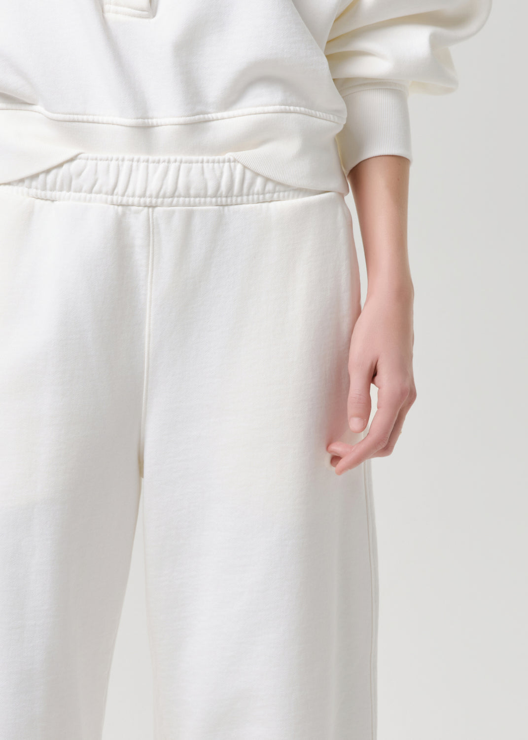 Close-up of a person wearing cream-colored sweatpants and a matching sweatshirt, showing the fabric texture and elastic waistband against a grey background.