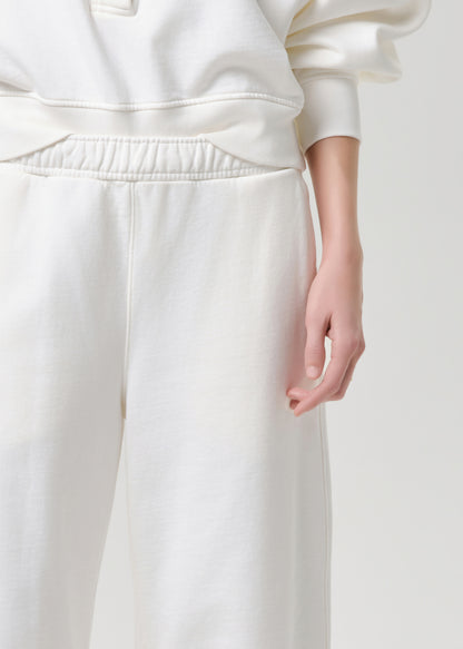Close-up of a person wearing cream-colored sweatpants and a matching sweatshirt, showing the fabric texture and elastic waistband against a grey background.