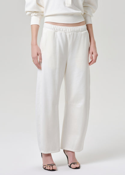 A model wearing off-white wide-leg cropped pants with an elastic waistband, paired with a matching cream sweatshirt and black heeled sandals, against a grey background.