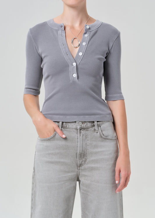 Person wearing a gray ribbed henley shirt and light gray jeans on a plain background