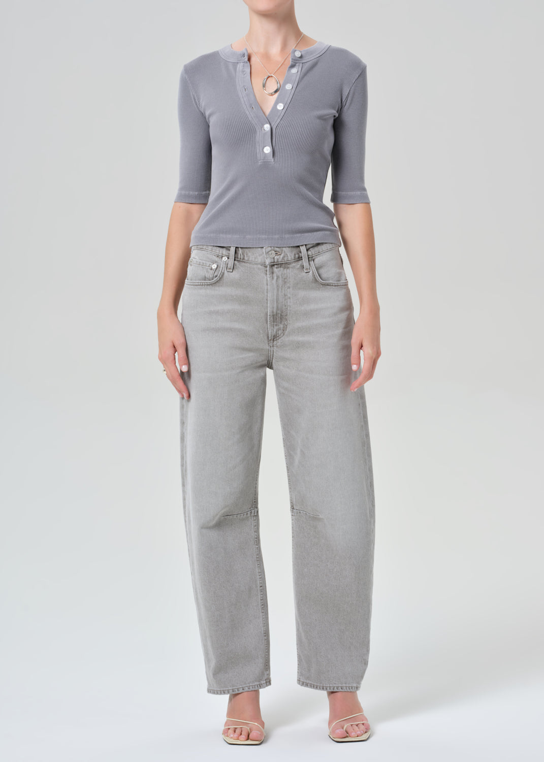 Person wearing a gray ribbed henley shirt and light gray jeans on a plain background