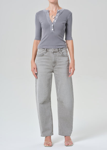 Person wearing a gray ribbed henley shirt and light gray jeans on a plain background