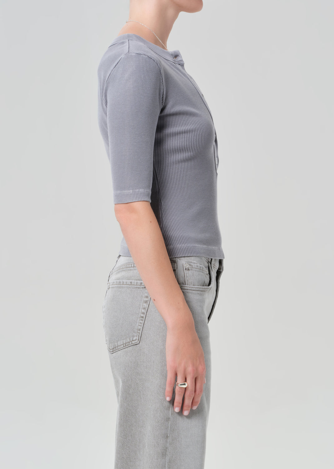Person wearing a gray ribbed henley shirt and light gray jeans on a plain background