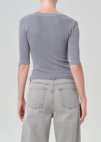 Person wearing a gray ribbed henley shirt and light gray jeans on a plain background