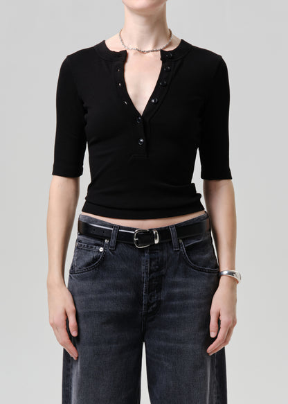 Person wearing a black short-sleeve top and dark jeans on a plain background