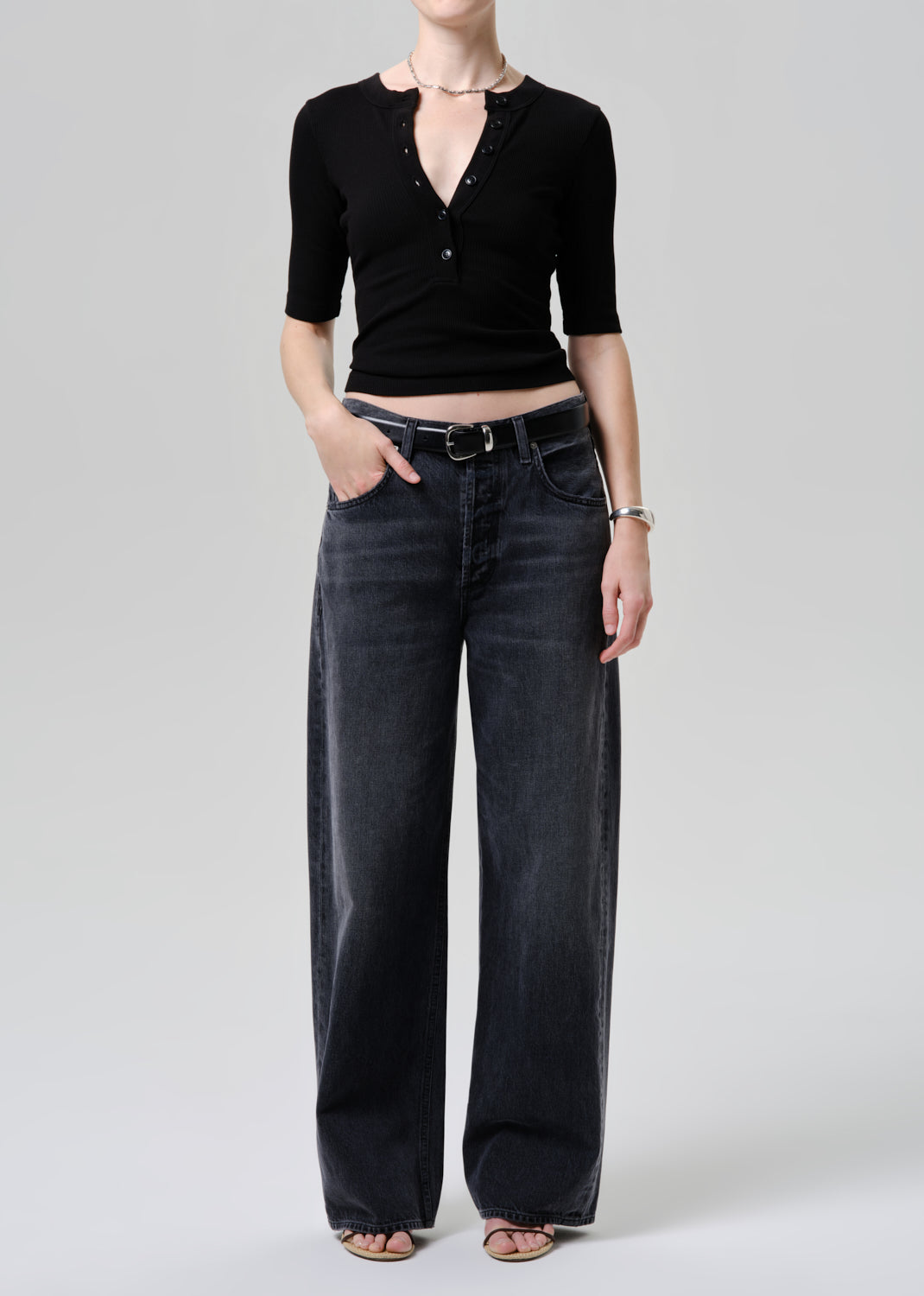 Person wearing a black top and washed black jeans on a grey background