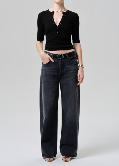 Person wearing a black top and washed black jeans on a grey background