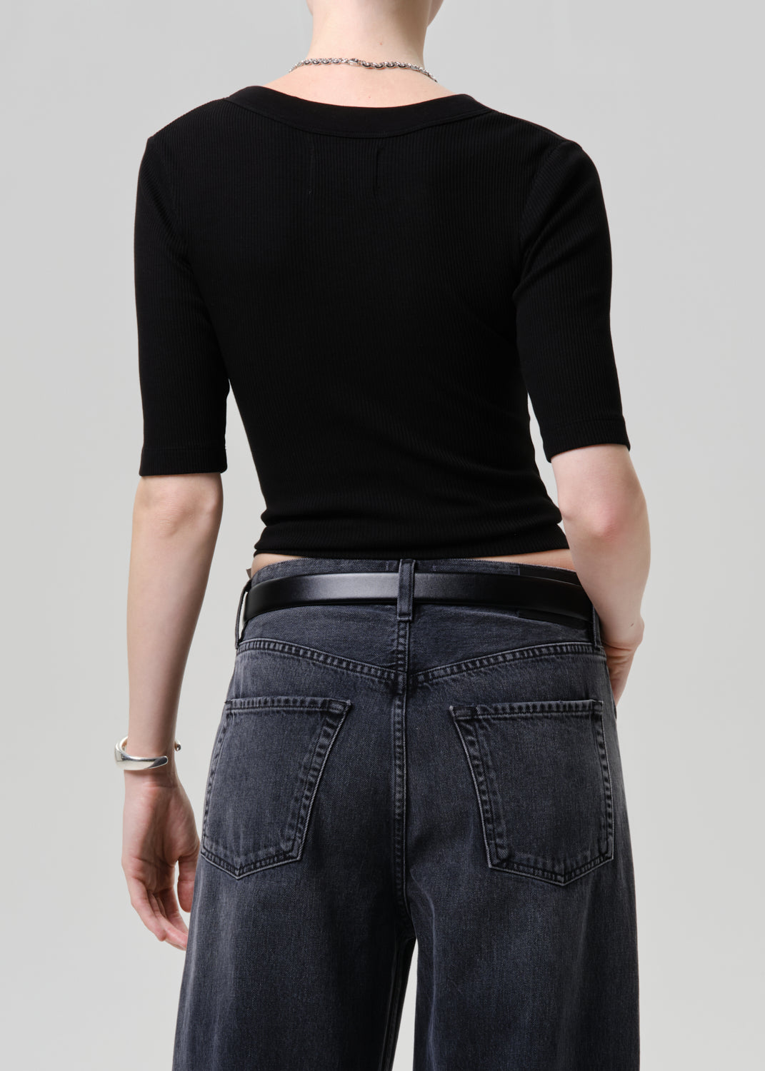 Person wearing a black crop top and dark jeans on a plain background
