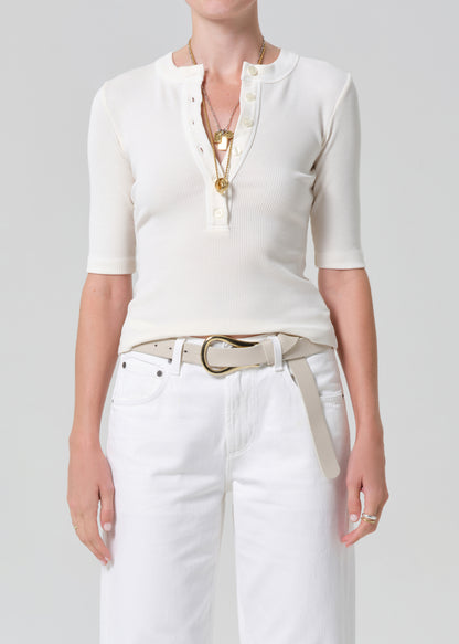Person wearing a white top and white pants with a belt on a plain background