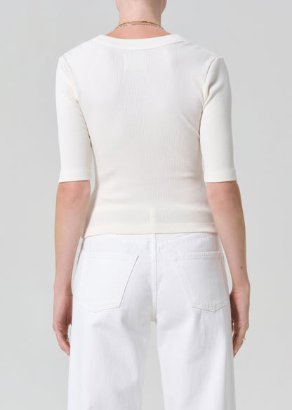 Person wearing a white top and white pants with a belt on a plain background
