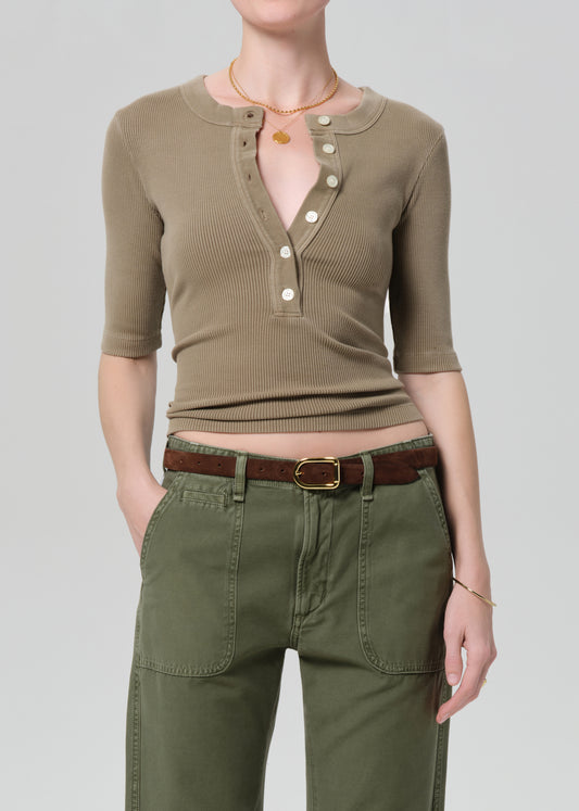 Person wearing a brown shirt and green pants on a plain background