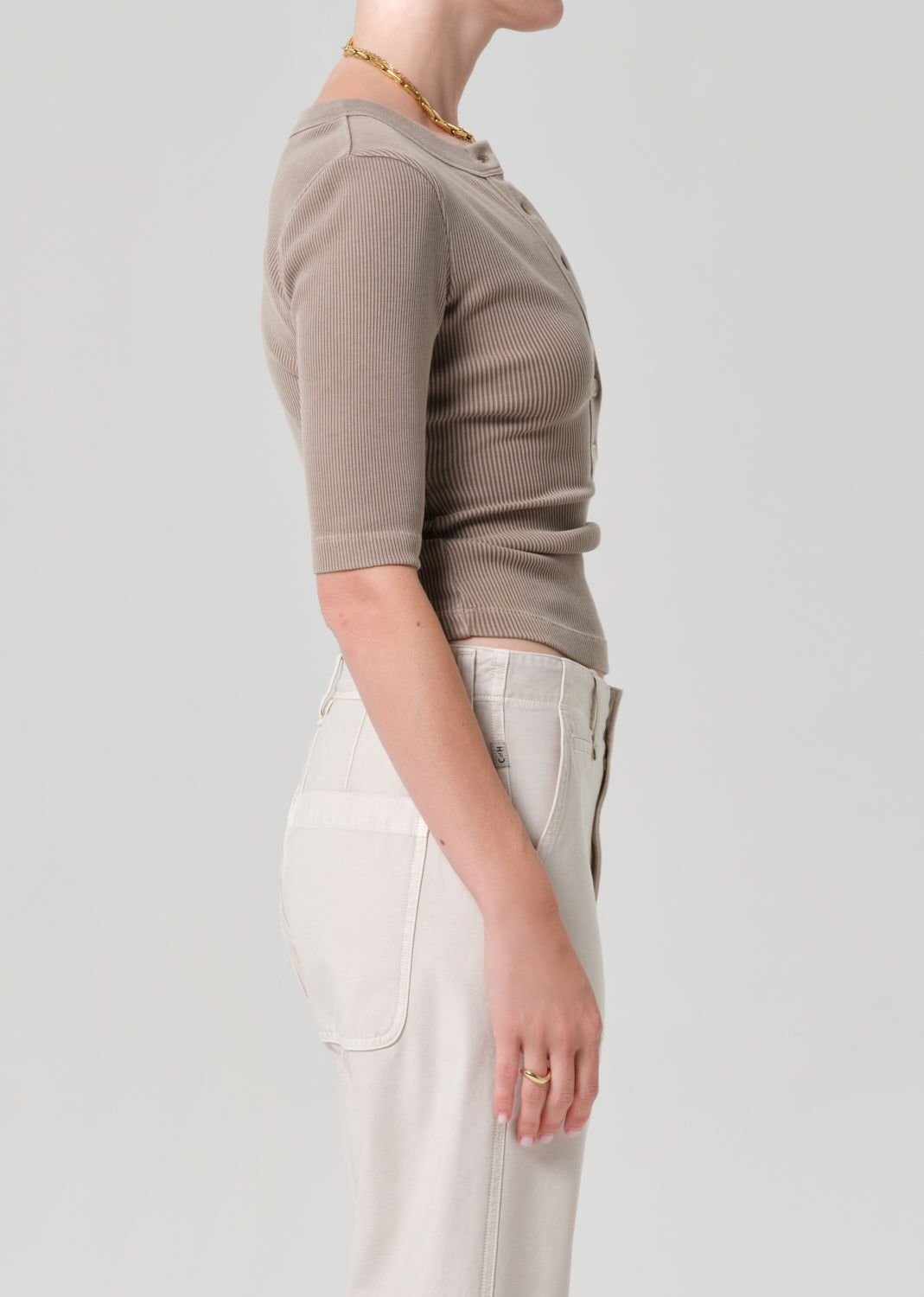 Person wearing a brown short-sleeve top and light-colored pants on a plain background