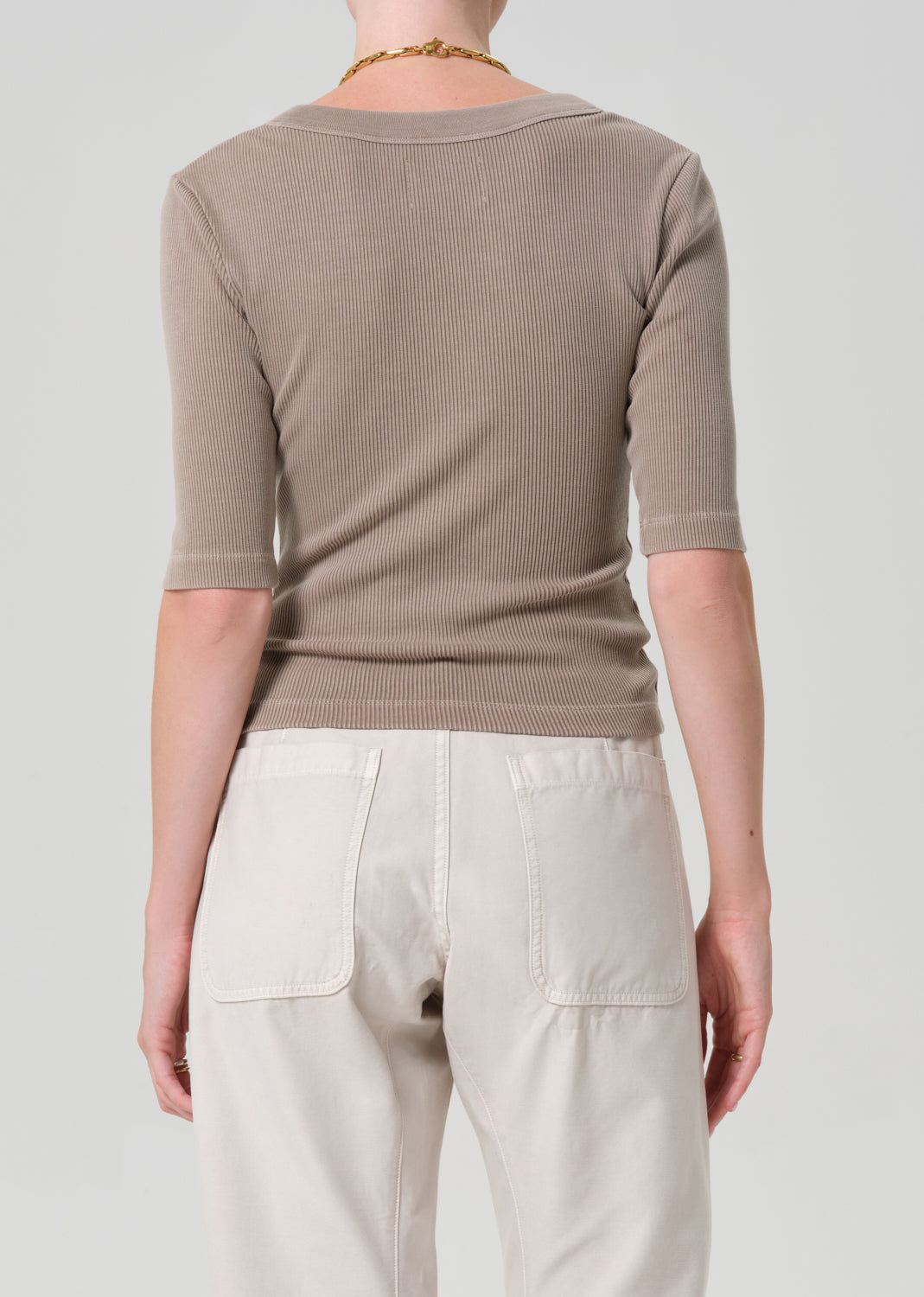 Person wearing a beige ribbed sweater and light-colored pants on a plain background