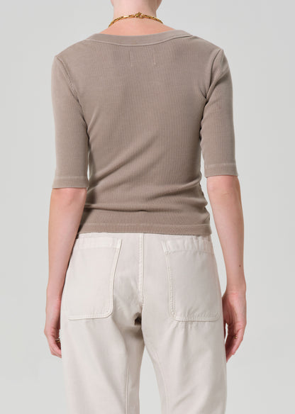 Person wearing a beige ribbed sweater and light-colored pants on a plain background