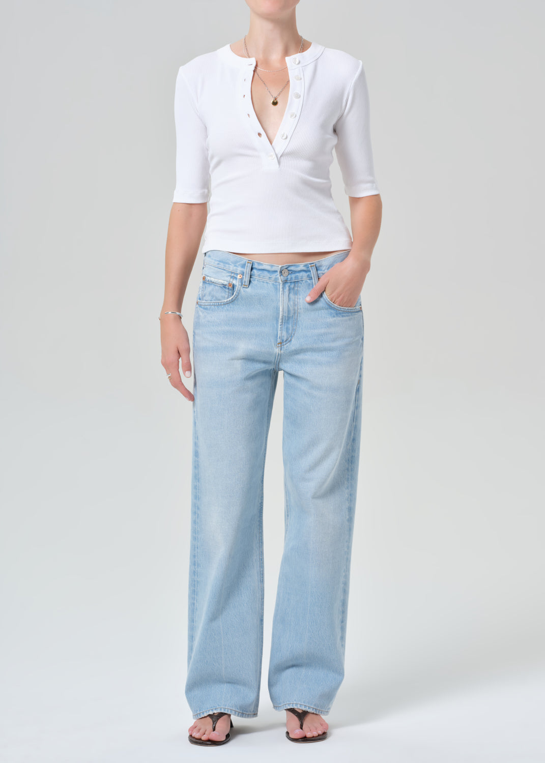 Person wearing a white short-sleeve shirt and light blue jeans on a gray background