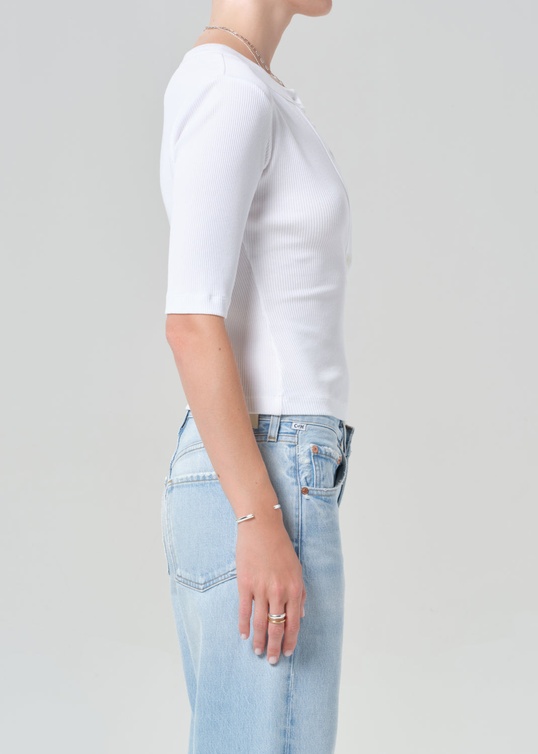 Person wearing a white short-sleeve shirt and light blue jeans on a gray background