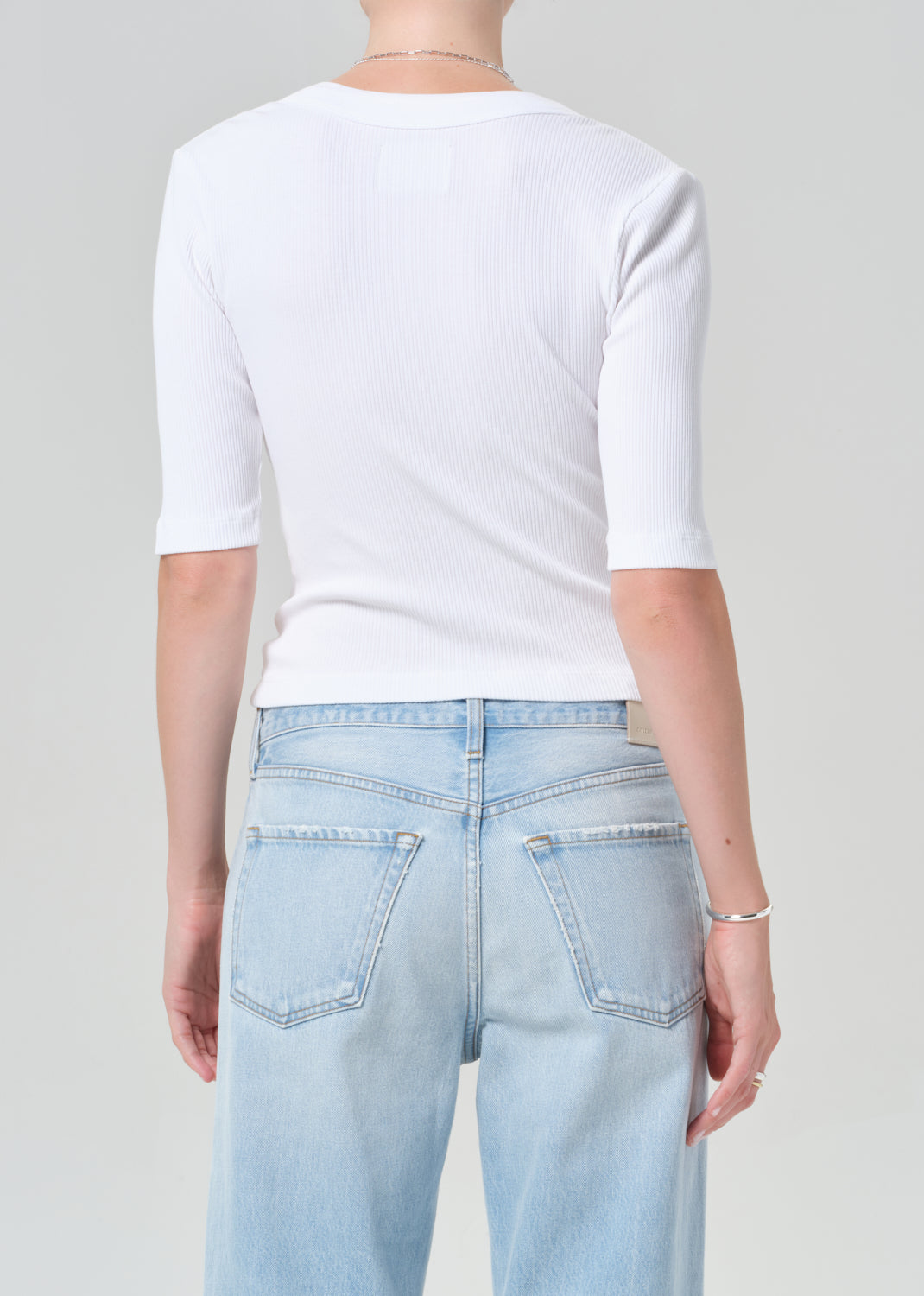 Person wearing a white short-sleeve shirt and light blue jeans on a gray background