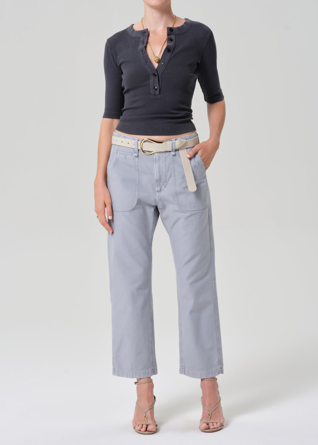 Person wearing a grey short-sleeve top and light gray pants with a beige belt on a plain background