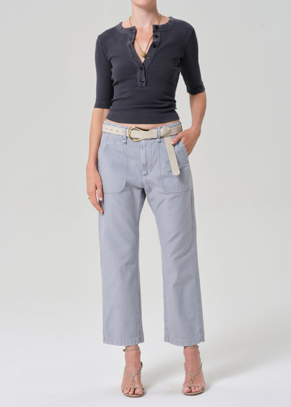 Person wearing a grey short-sleeve top and light gray pants with a beige belt on a plain background