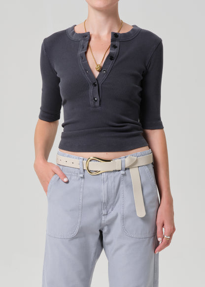 Person wearing a GREY short-sleeve top and light gray pants with a beige belt on a plain background