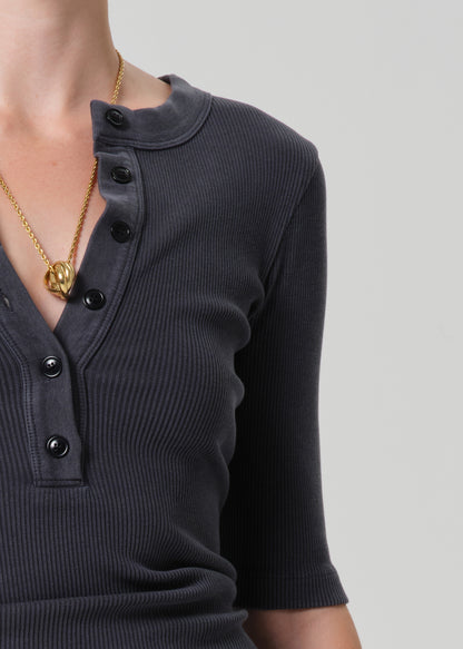 Person wearing a grey short-sleeve top and light gray pants with a beige belt on a plain background