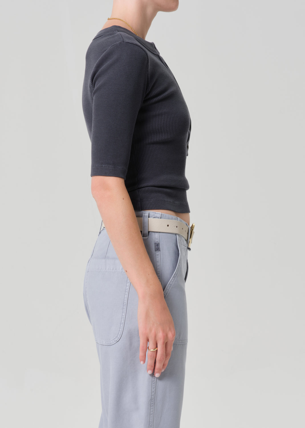 Person wearing a GREY short-sleeve top and light gray pants with a beige belt on a plain background