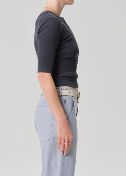 Person wearing a GREY short-sleeve top and light gray pants with a beige belt on a plain background