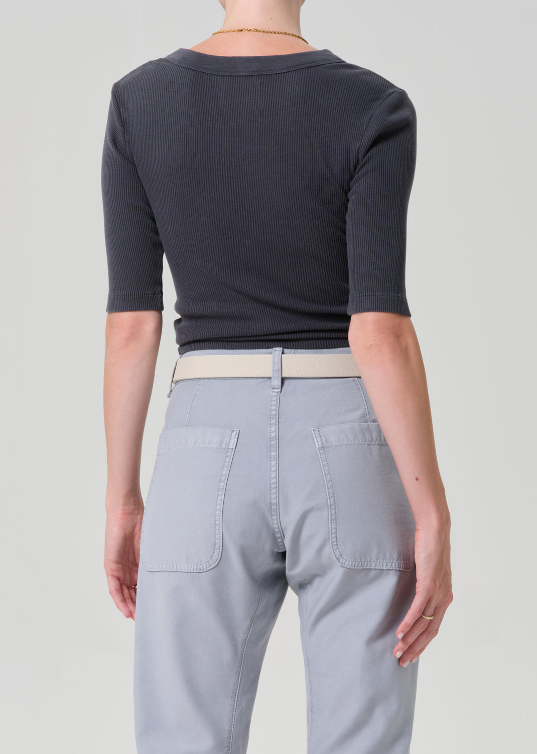 Person wearing a GREY short-sleeve top and light gray pants with a beige belt on a plain background