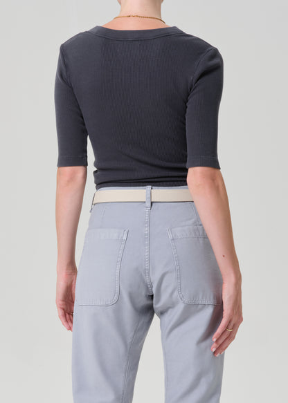 Person wearing a GREY short-sleeve top and light gray pants with a beige belt on a plain background