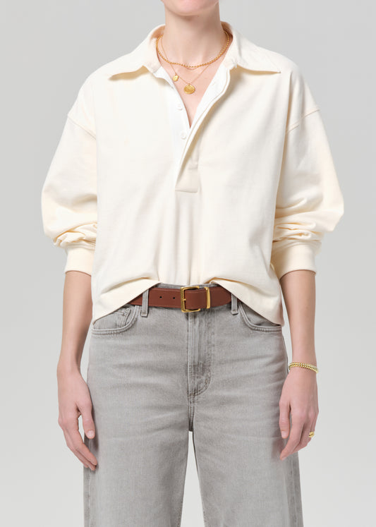 Person wearing a cream rugby with gold trim and light gray jeans on a plain background