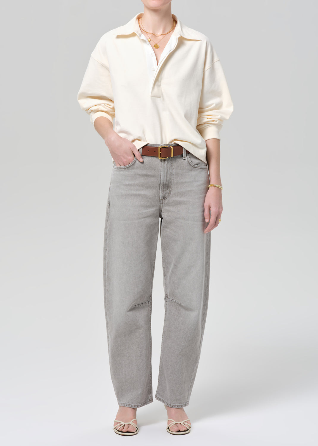 Person wearing a cream rugby with gold trim and light gray jeans on a plain background