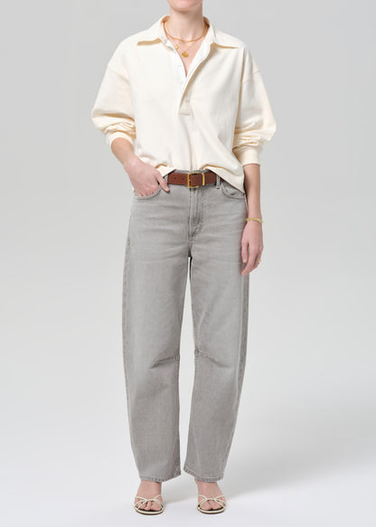Person wearing a cream rugby with gold trim and light gray jeans on a plain background